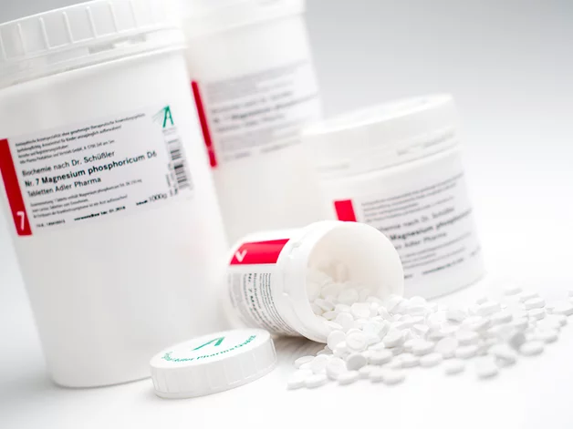Mehrere Dosen Schüßler Salz, eine geöffnet mit verstreuten Tabletten, in weißer Verpackung